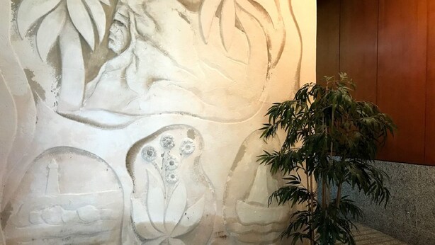 En væg med et blomsterrelief, en potteplante og en stenbænk.