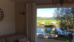 Ein Zimmer mit einer Couch und einem Fenster mit Blick auf einen Teich mit Kühen.