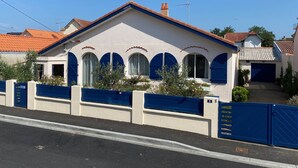 Una casa con fachada blanca, contraventanas azules y techo de tejas rojas.
