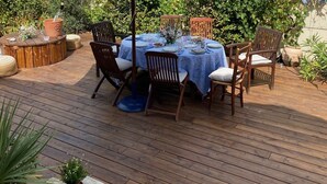 Un patio al aire libre con una mesa redonda, una sombrilla azul y sillas de madera.