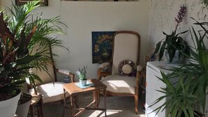 Un patio iluminado por el sol con mesa, sillas, plantas en macetas, un refrigerador y una ventana con vista a un edificio.