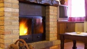 A stone fireplace with a television on top, a wooden table, and a basket of pinecones. - Apartment 4 guests in Casa Serra de Dalt (Lladurs)