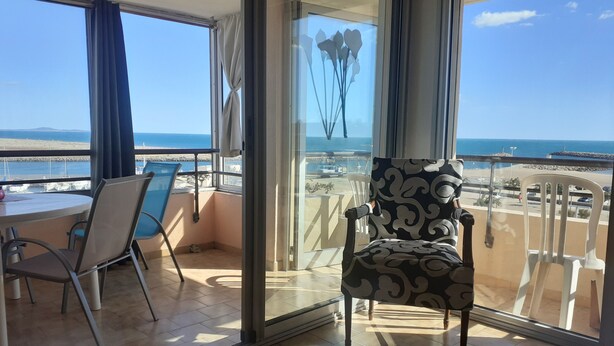 Un balcón con vista a la playa, una mesa de comedor con sillas y un sillón estampado.