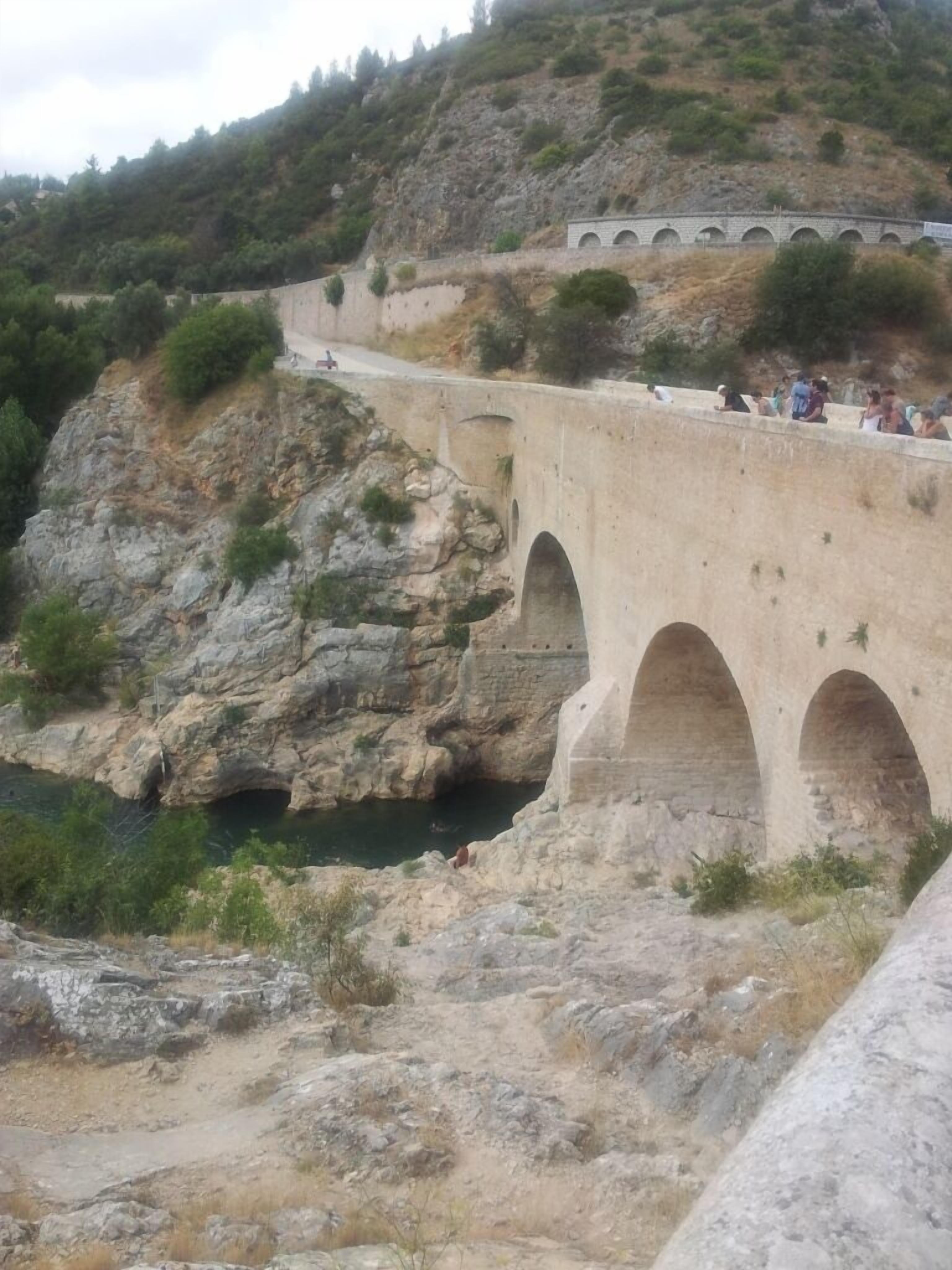 A stone bridge with multiple arches over a rocky terrain and a body of water.