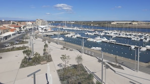 Un puerto deportivo con barcos amarrados, un paseo para peatones y edificios al fondo.