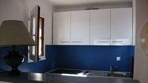 Una cocina compacta con armarios blancos, un salpicadero azul y un lavabo.