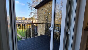 A balcony with a black metal railing, a small table with a chair, and a view of a brick wall and a grassy area with solar panels in the background. - Large sunny fresh two bedroom apt in London ideal for tourists, refurbished  (London)