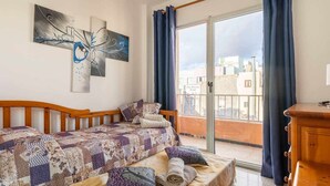 Un dormitorio con cama, cabecero de madera, ventana con cortinas y vista a edificios.