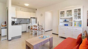 Un espacio habitable compacto con kitchenette, comedor y una pequeña sala de estar con sofá y mesa.