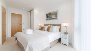 Un dormitorio ordenado con una cama, mesitas de noche y un cuadro en la pared.