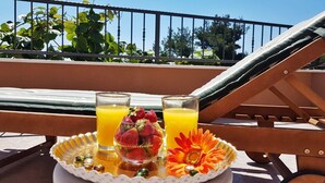 Un balcón con una mesa que sostiene dos vasos de jugo de naranja, un tazón de fresas y una flor decorativa.