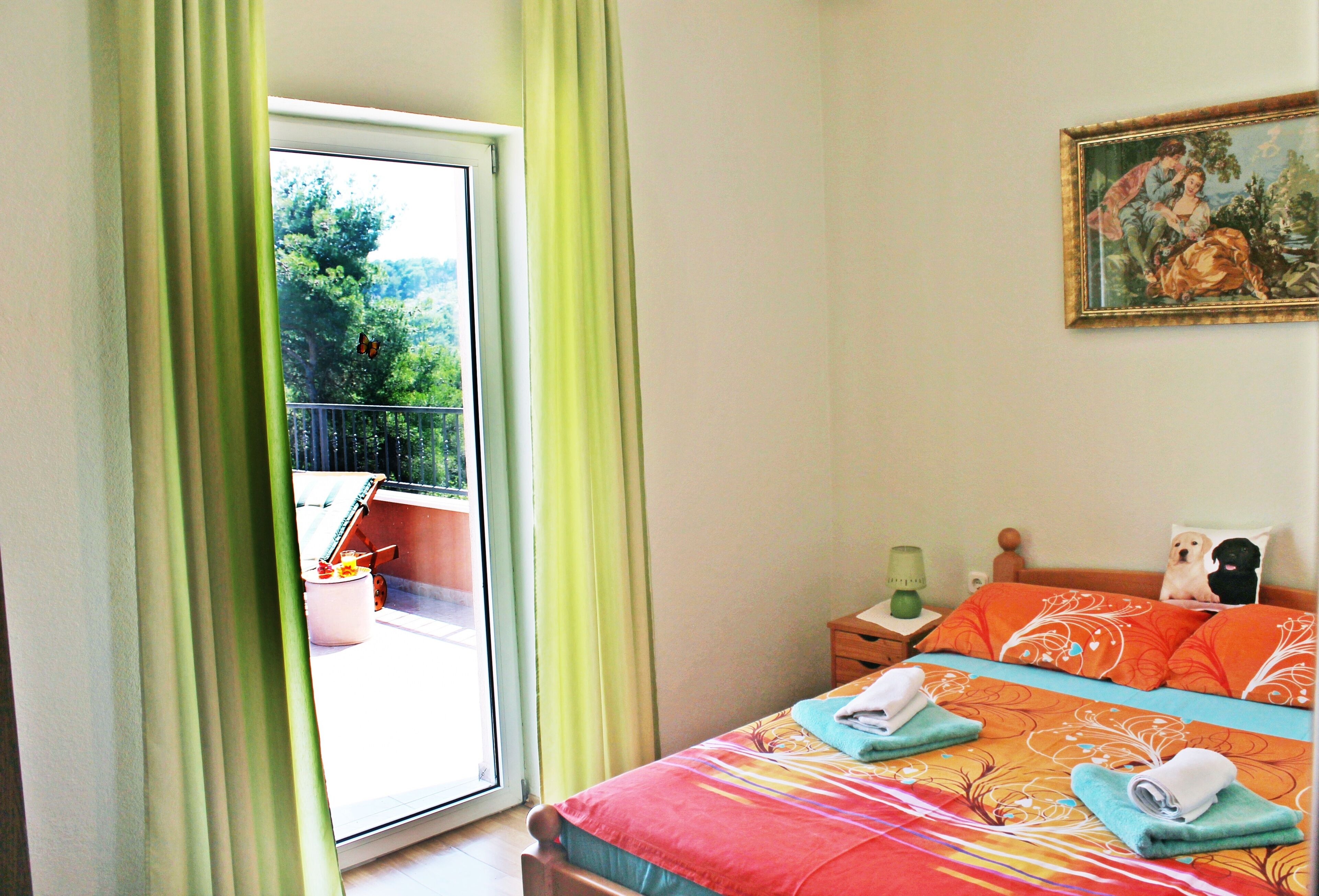 Un dormitorio con cama, un cuadro en la pared y vistas al exterior con vegetación.