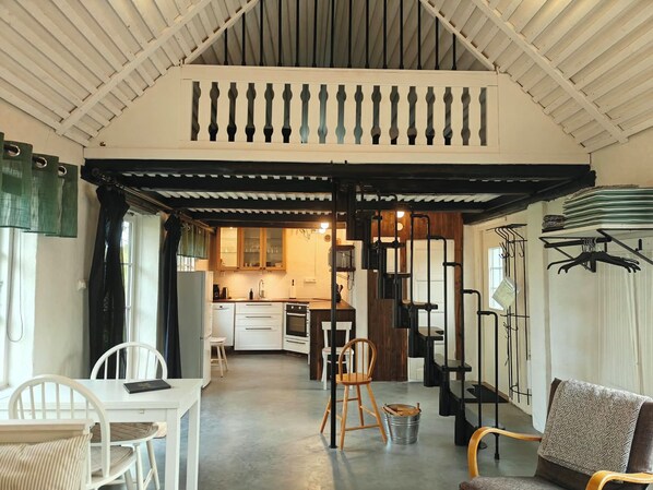 A spacious kitchen with wooden cabinets, a dining area with white furniture, and a staircase leading to an upper level. - Charming cottage on a farm (Ystad V)