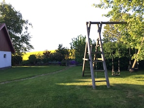 A wooden swing set in a grassy yard with a red barn in the background.