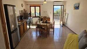 A compact kitchen with a dining area, a refrigerator, a stove, and a window with curtains. - OLMETO, F2 air-conditioned, near sea (Olmeto)