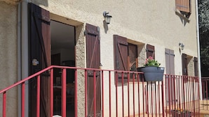 A building with a red metal railing, open wooden doors, and potted plants on the balcony. - OLMETO, F2 air-conditioned, near sea (Olmeto)