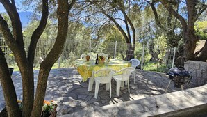 An outdoor patio with a stone table and white chairs, surrounded by trees and a metal fence. - OLMETO, F2 air-conditioned, near sea (Olmeto)