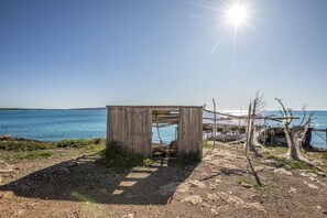A small wooden structure with a door, situated on a rocky shore with a view of the sea. - Country Cottage / Gite - SAN FRANCISCO JAVIER FORMENTERA (Sant Francesc de Formentera)