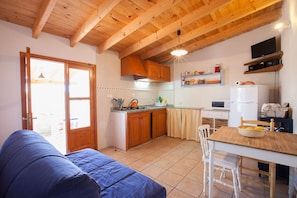 A compact kitchen with wooden cabinets, a dining table, and a sofa in a cozy room. - Country Cottage / Gite - SAN FRANCISCO JAVIER FORMENTERA (Sant Francesc de Formentera)