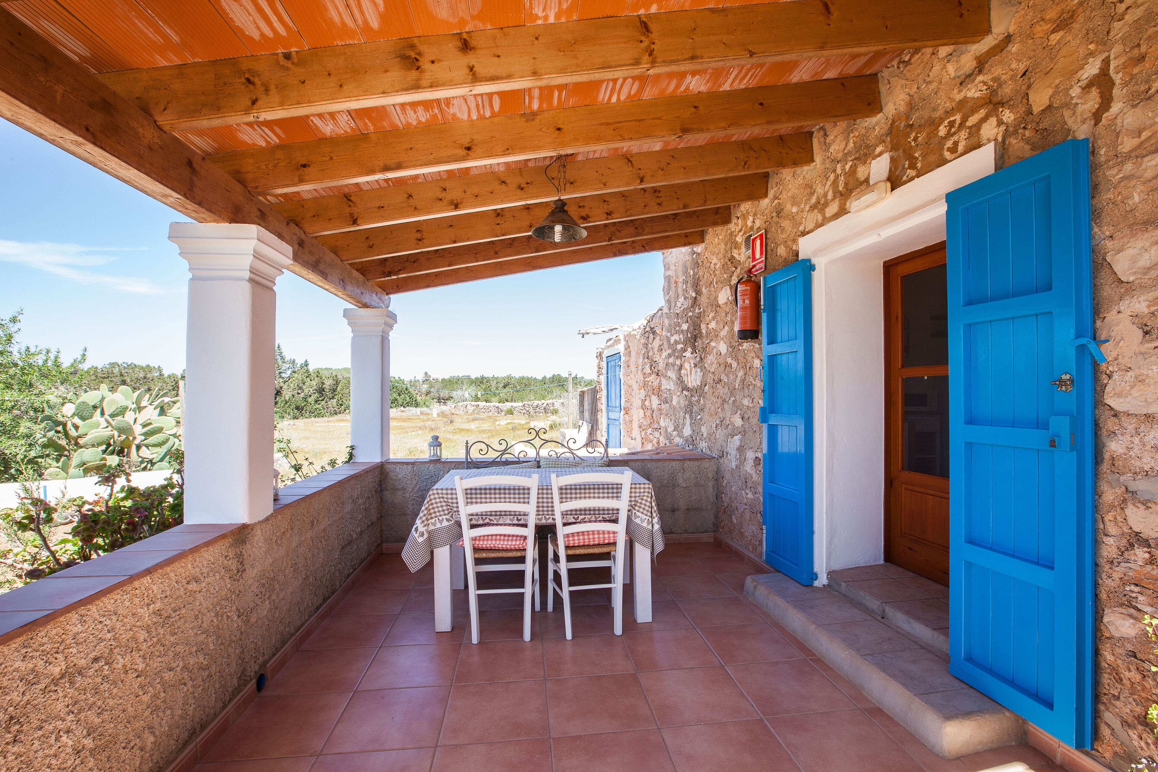 Un patio cubierto con una mesa y sillas, un muro de piedra y una puerta azul.