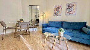 Ett modernt vardagsrum med en blå soffa, ett soffbord i glas och en matplats med stolar och ett bord.