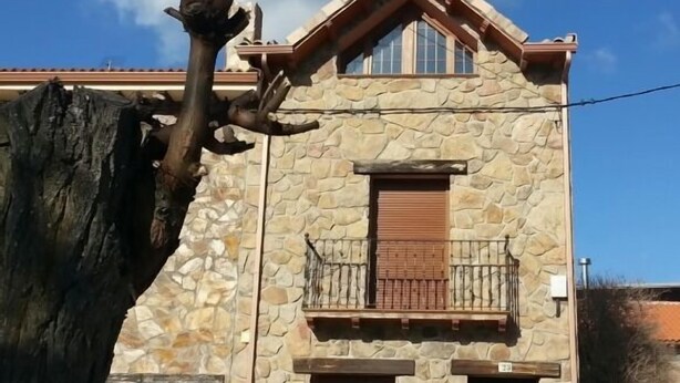 A stone building with a balcony and a large tree in front.