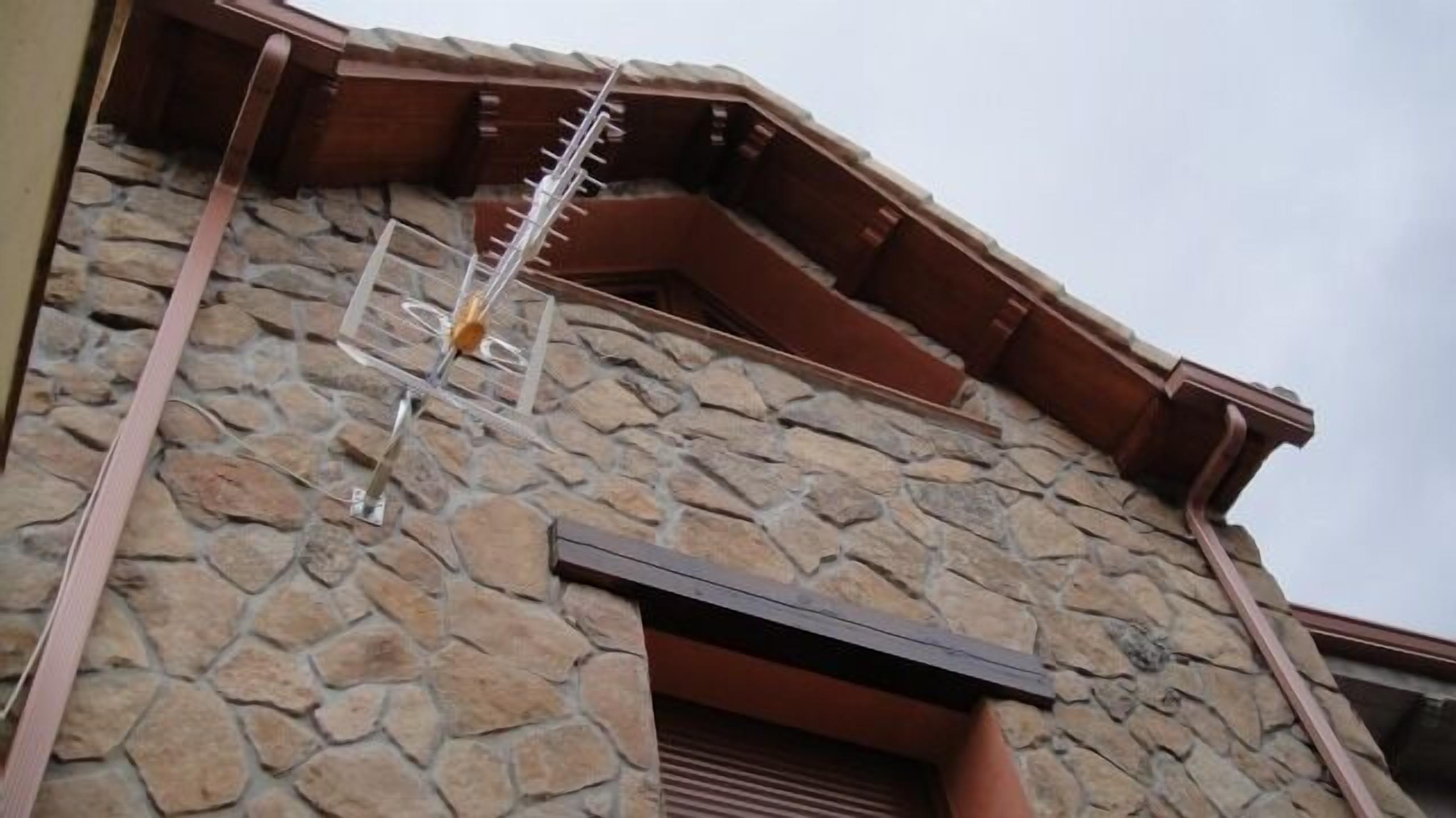 Un edificio de piedra con techo inclinado y una escalera de metal que conduce a una terraza de madera.