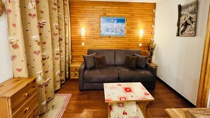A cozy living room with a wooden wall panel, a grey sofa, a small table, and a painting. - Vacations in Belle Plagne at the foot of the slopes (Saturday to Saturday rentals) (Belle-Plagne)