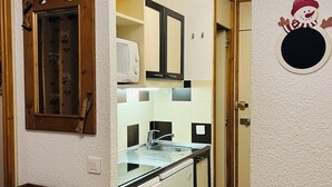 A compact kitchen with a microwave, sink, and dishwasher. There's a wooden cabinet with a mirror and a small wooden table. A wooden chair is visible in the foreground. - Vacations in Belle Plagne at the foot of the slopes (Saturday to Saturday rentals) (Belle-Plagne)