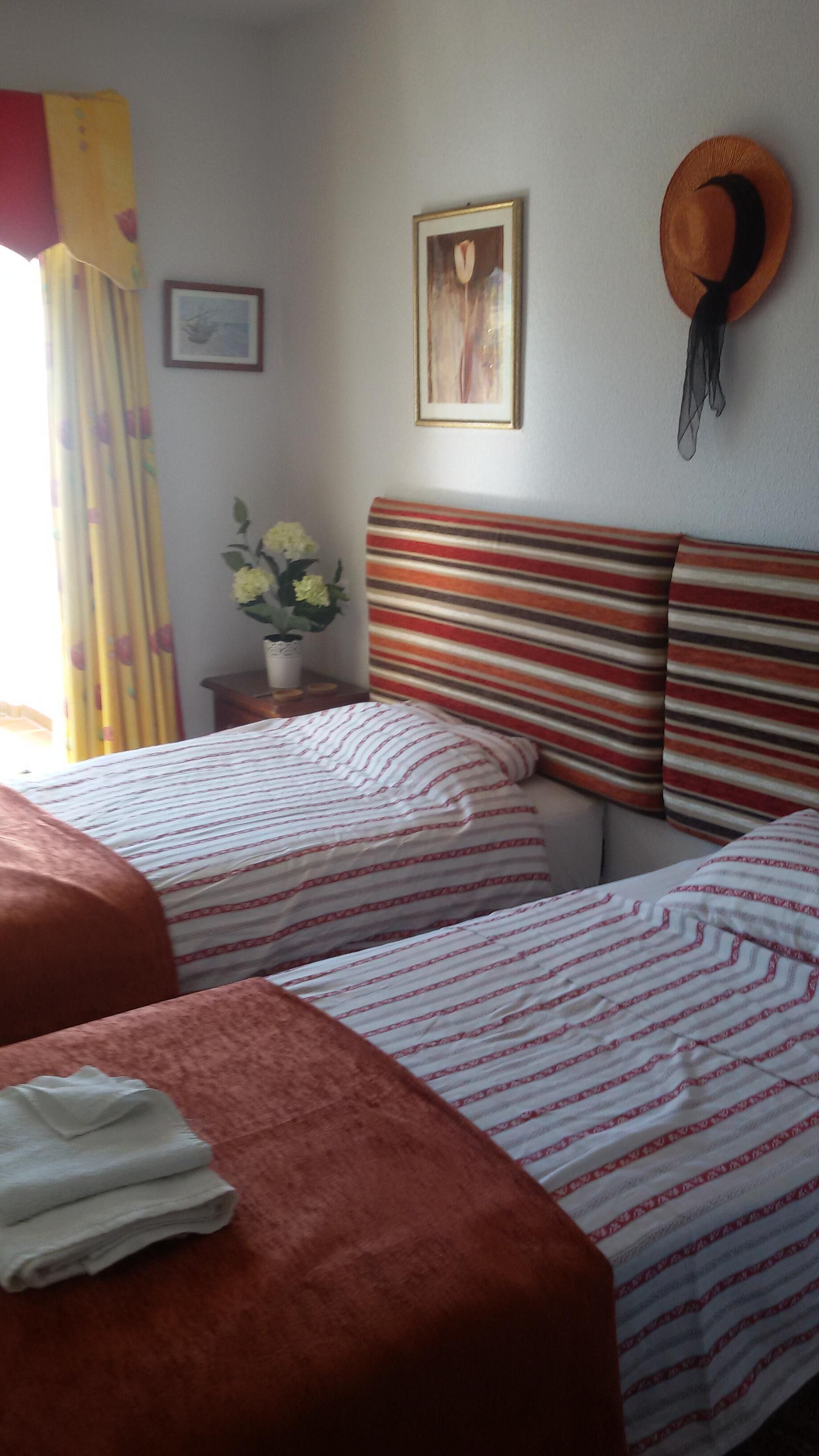Habitació d'hotel amb dos llits, un capçal de llit estriat, un quadre amb marc i un barret penjat a la paret.