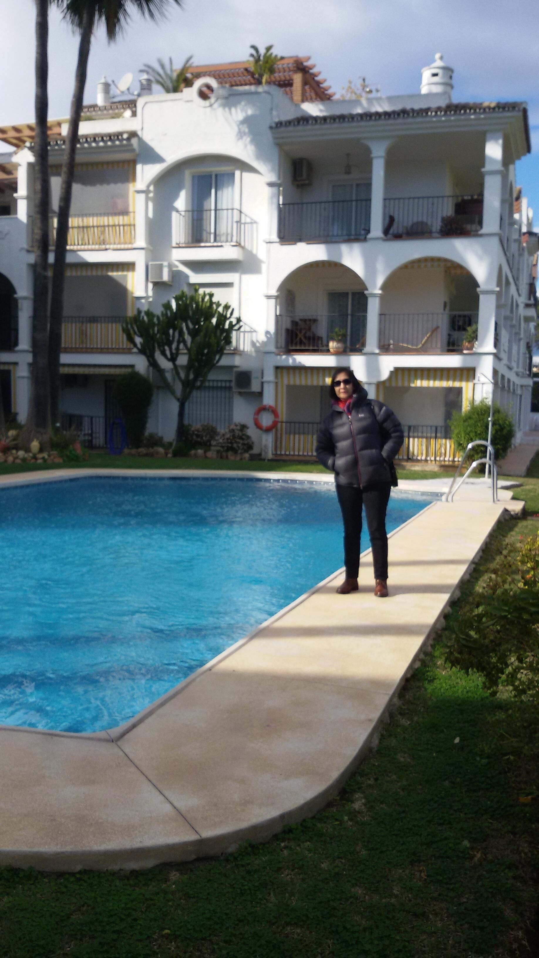 A person standing by a swimming pool with a multi-story building in the background.