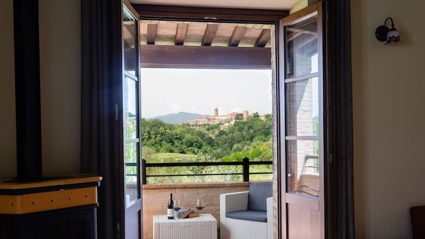 A balcony with a wicker table, a chair, and a bottle of wine.