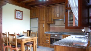 A kitchen with wooden cabinets, a granite countertop, and a dining table with chairs. - Casa para 5 en el centro de Colombres (Colombres)