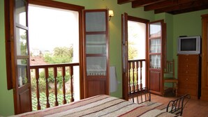 A bedroom with a bed, a television, and a balcony with a view of greenery. - Casa para 5 en el centro de Colombres (Colombres)