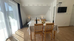 Ein gemütliches Zimmer mit einem Bett, einem Esstisch mit Stühlen, einem an der Wand montierten Fernseher und einem Fenster mit Vorhängen.