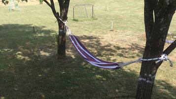 A hammock tied between two trees in a grassy area with a soccer goal in the background.