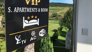 S. Apartments & Room Schild mit einem Wappenlogo, Bettsymbol, Fernsehersymbol, Klimaanlagensymbol und WLAN-Symbol.