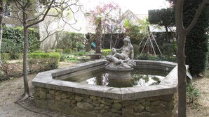 Una fuente de piedra con una estatua de una figura sentada, rodeada por un muro de piedra y follaje.