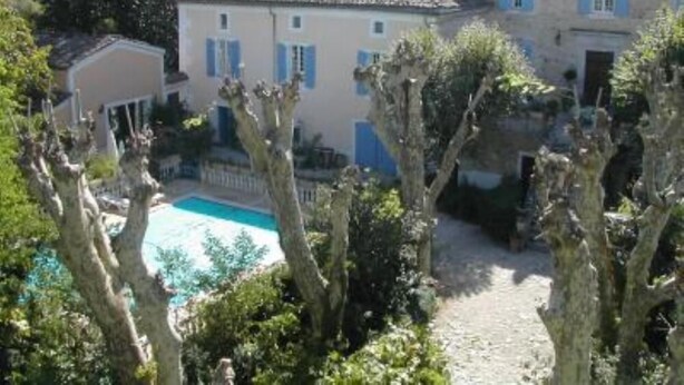 Un edificio con piscina, rodeado de árboles y colinas.