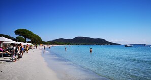 A beach with clear blue water, people swimming, and umbrellas on the sand.