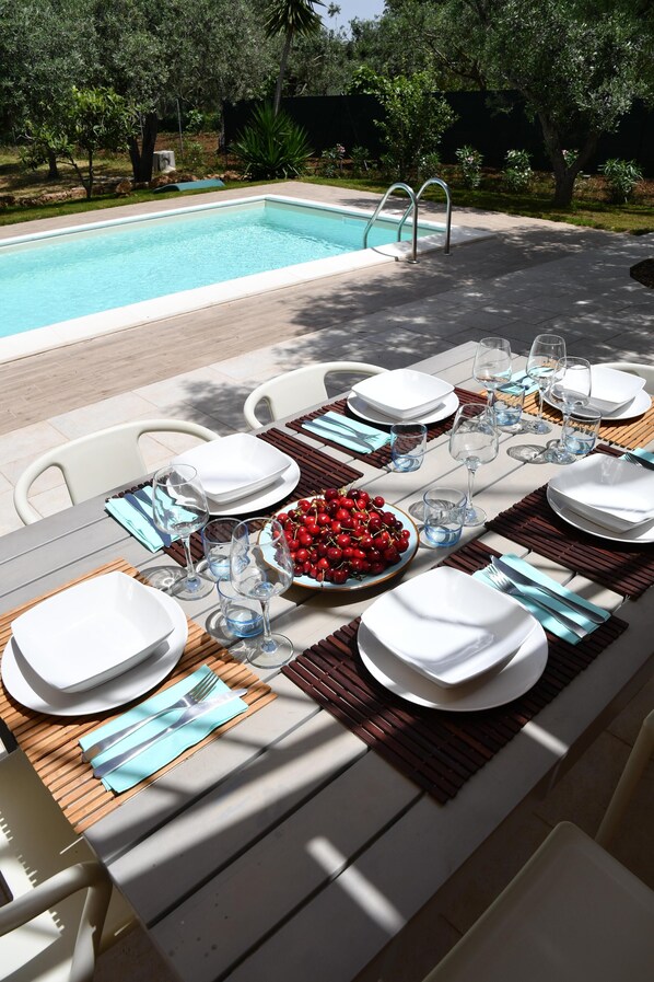 An outdoor dining area with a pool in the background. - Villa with pool surrounded by olive groves. With sea view.Casa in campagna. (Alghero)