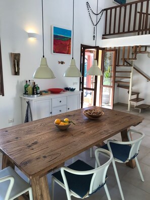A dining area with a wooden table, white chairs, pendant lights, and a view of a staircase.