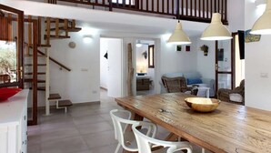 A spacious kitchen with a wooden table, white chairs, and pendant lights. A staircase leads to an upper level. - Villa with pool surrounded by olive groves. With sea view.Casa in campagna.  (Alghero)