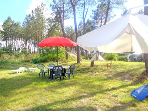 Ein Campingplatz mit Tisch und Stühlen unter einem roten Sonnenschirm, umgeben von Bäumen und einem Zelt.