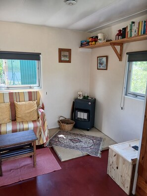 A cozy room with a sofa, a small table, a heater, a bookshelf, and a window.