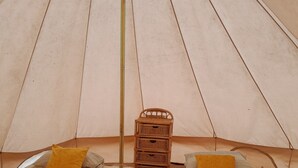 Due letti con cuscini, un piccolo scrigno in legno e un tappeto a righe in una stanza simile a una tenda.