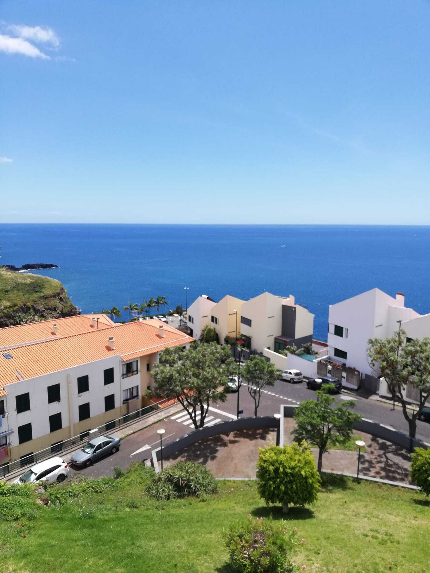 Zona residencial costera con edificios modernos, cielo azul despejado y el océano al fondo.