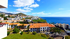 Ein Küstenwohngebiet mit Häusern mit Terrakotta-Dachziegeln, einem klaren blauen Himmel und Blick auf den Ozean.