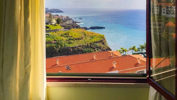 Ein Fenster mit Blick auf eine Küstenlandschaft, einschließlich eines Gewässers und Gebäuden in der Ferne.
