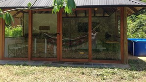 Une structure entièrement vitrée, dotée d’un toit en métal, de poutres en bois et d’un hamac à l’intérieur.